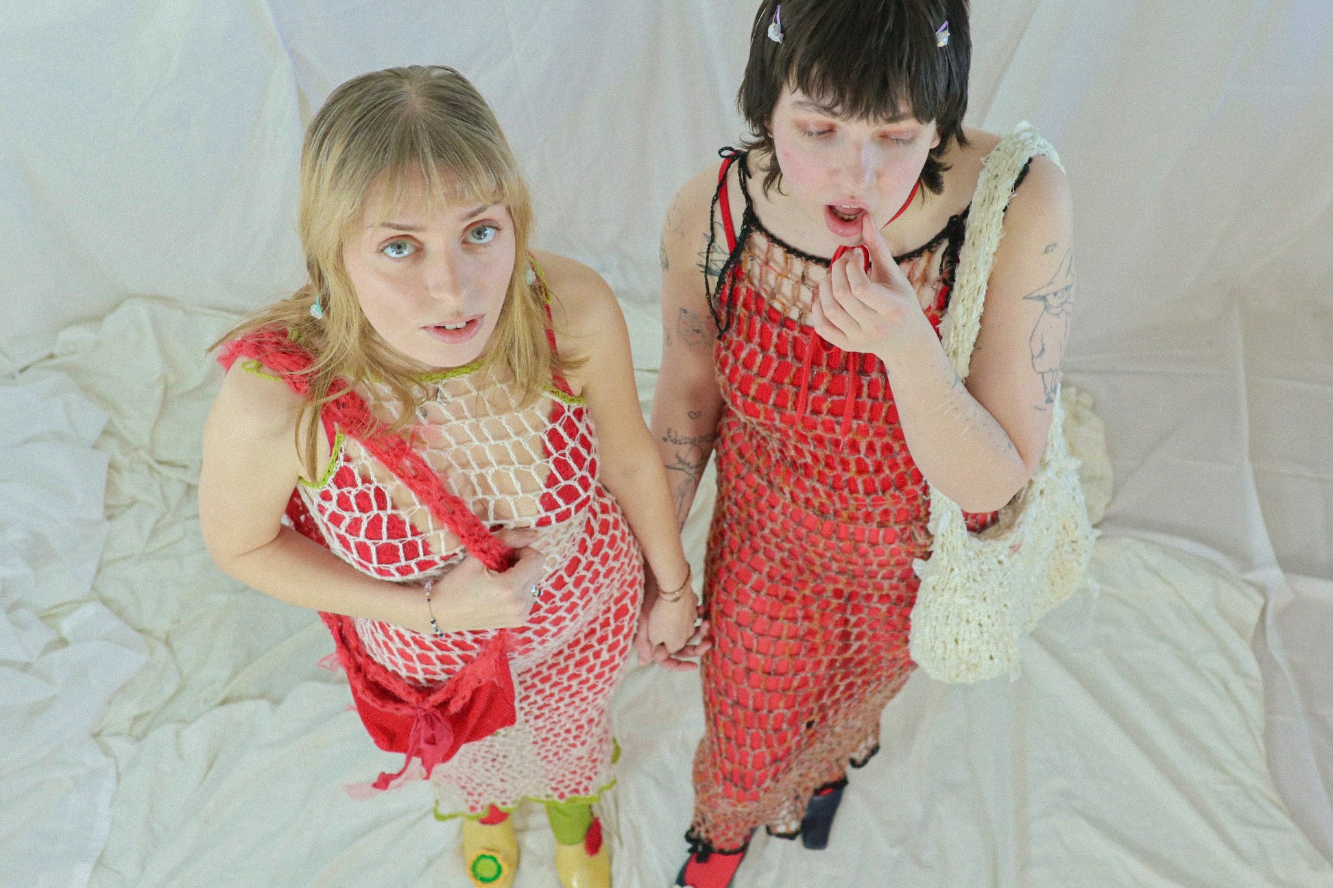 Two people wearing red and white crochet outfits against a white background