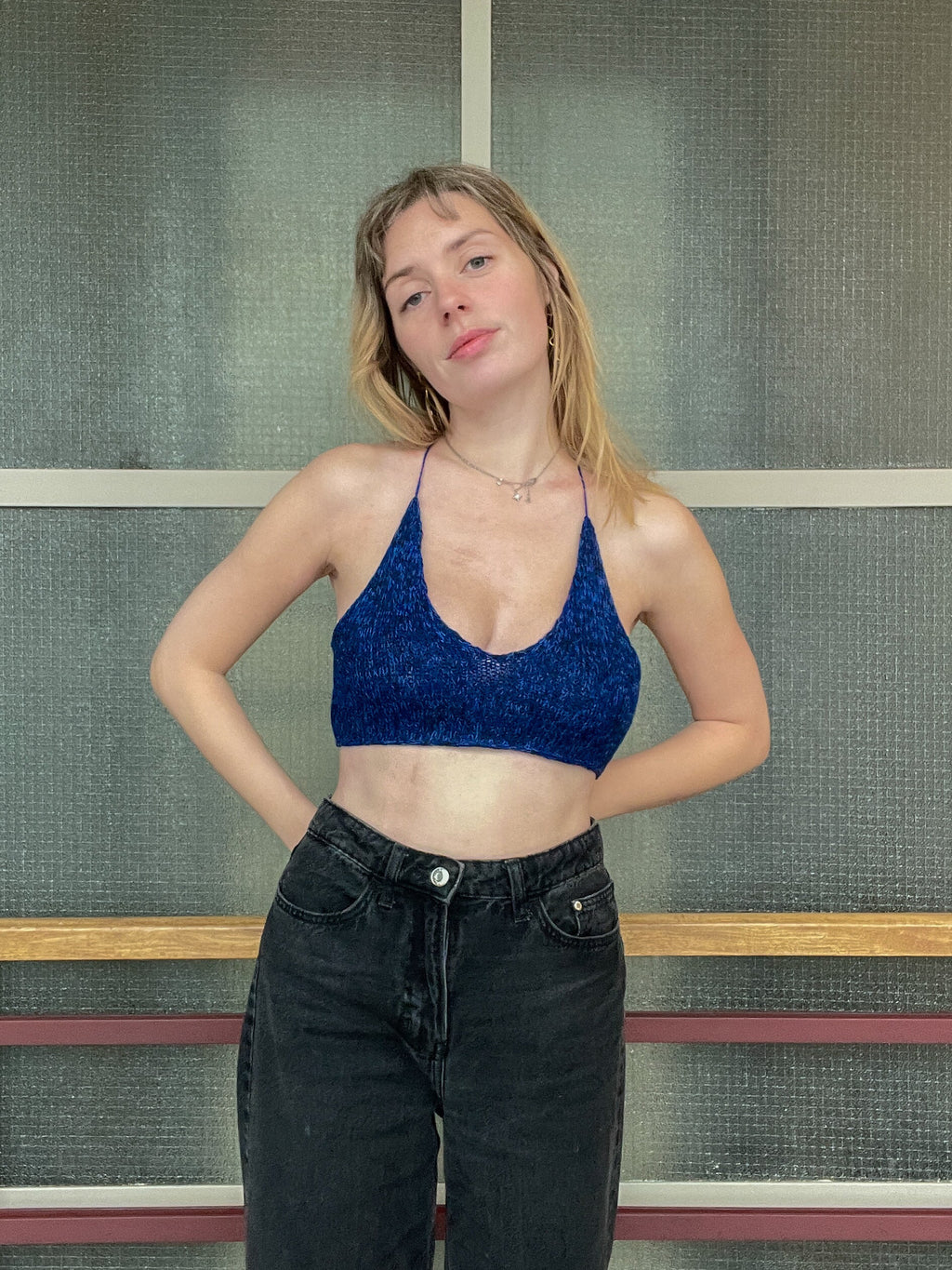 Woman wearing a blue top and black pants standing against a textured wall.