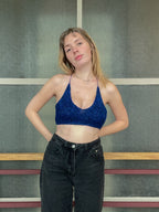 Woman wearing a blue top and black pants standing against a textured wall.