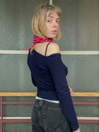 Woman wearing a navy blue top and black pants with a pink scarf, standing in front of a textured wall.